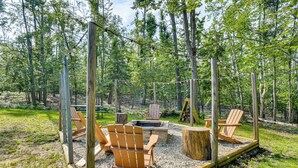 Een terras met Adirondack-stoelen, een vuurkorf en een houten terras, omgeven door bomen.