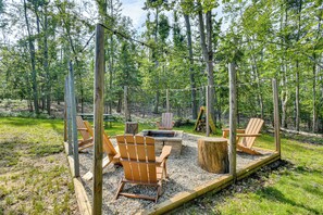An outdoor seating area with Adirondack chairs, a fire pit, and a wooden deck surrounded by trees. - 'The Blue Goose Chalet': Your Cozy Up North Escape (Gaylord)