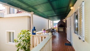 A covered outdoor balcony with a table and chairs, a lantern, and a potted plant. - Apartments Rasica Molunat - One Bedroom Apartment (Konavle)