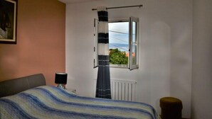 Ein Schlafzimmer mit einem Bett, einem Fenster mit Vorhängen, einem Heizkörper und einem Bild an der Wand.
