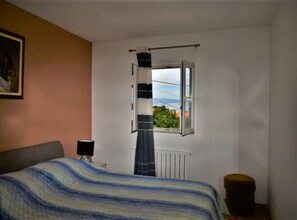 Ein Schlafzimmer mit einem Bett, einem Fenster mit Vorhängen, einem Heizkörper und einem Bild an der Wand.
