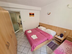 A hotel room with a bed, a nightstand, a lamp, a wall-mounted light, and a door leading to another room. - Apartments Pansion Franka 3 - Apartment 9 (Gradac)