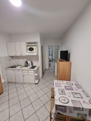 A compact kitchen with white cabinets, a microwave, and a coffee machine. There's a small table with a patterned tablecloth and a television on a wooden stand. - Apartments Pansion Franka 3 - Apartment 9 (Gradac)