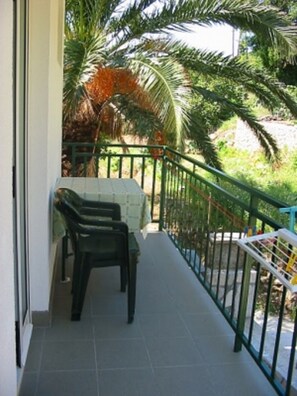 A balcony with a table and chairs, surrounded by a metal railing and palm trees. - Apartments Pansion Franka 3 - Apartment 9 (Gradac)
