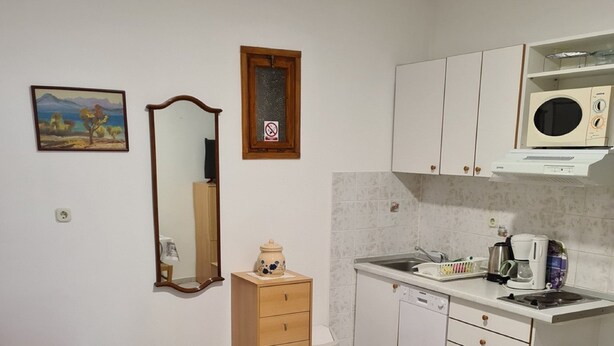 Een kleine kamer met een bed, een kitchenette, een spiegel en een schilderij aan de muur.