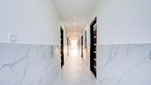 A corridor with marble walls and doors, leading to a bright room at the end. - Collection O Brookefield Central (Bengaluru)