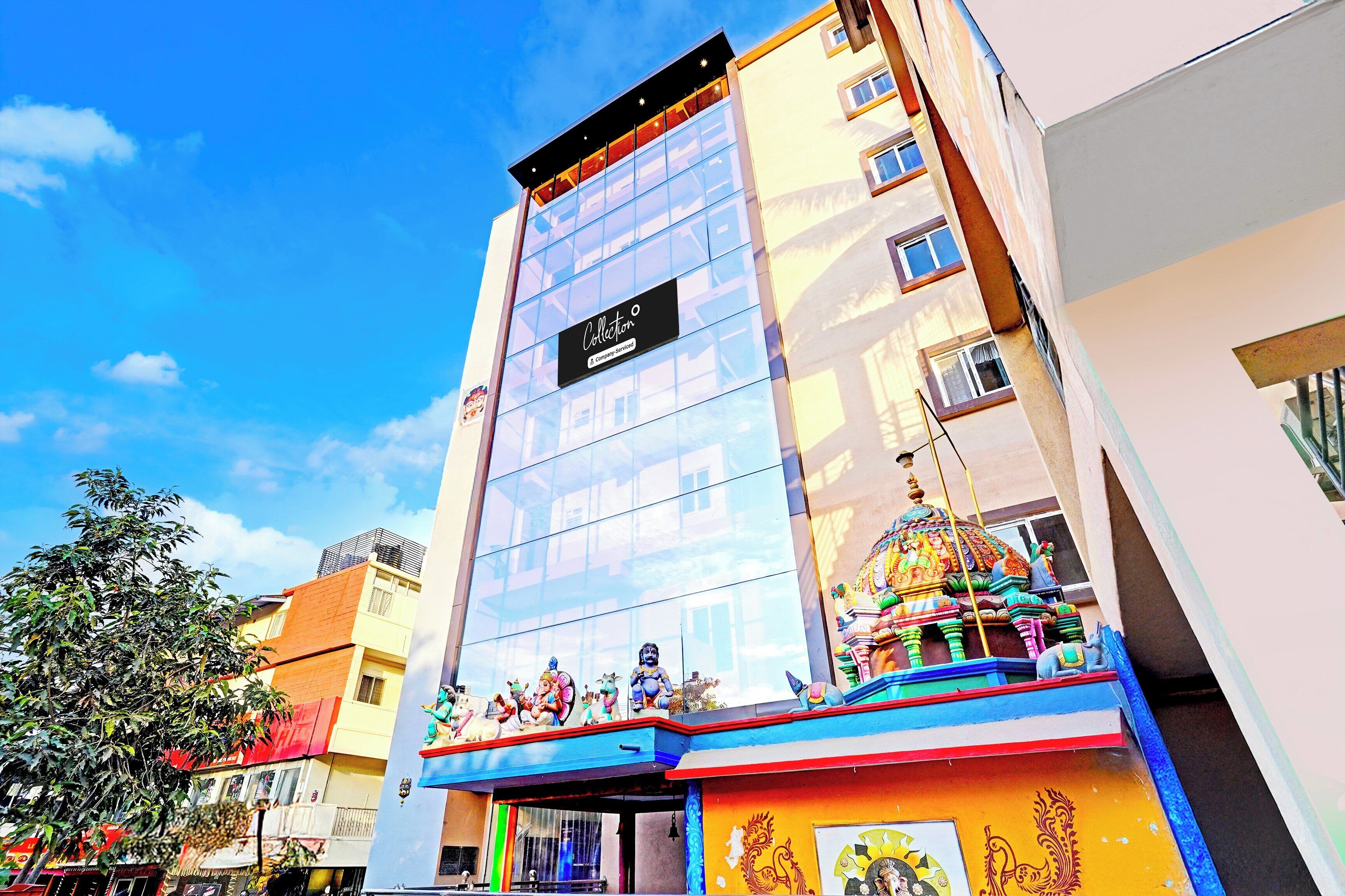 A hotel with a glass facade, a sign reading 'Collection', and a colorful entrance with statues.