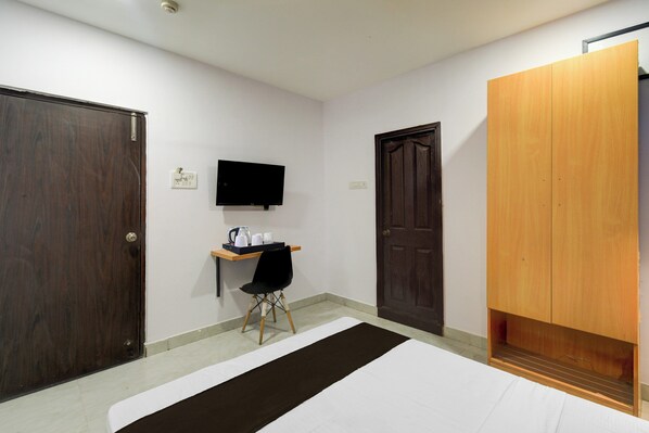 Una habitación de hotel con cama, escritorio con silla, televisor en la pared y dos puertas.