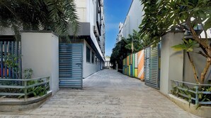 Uma passagem estreita ladeada por edifícios, com portões de metal e alguns espaços verdes.