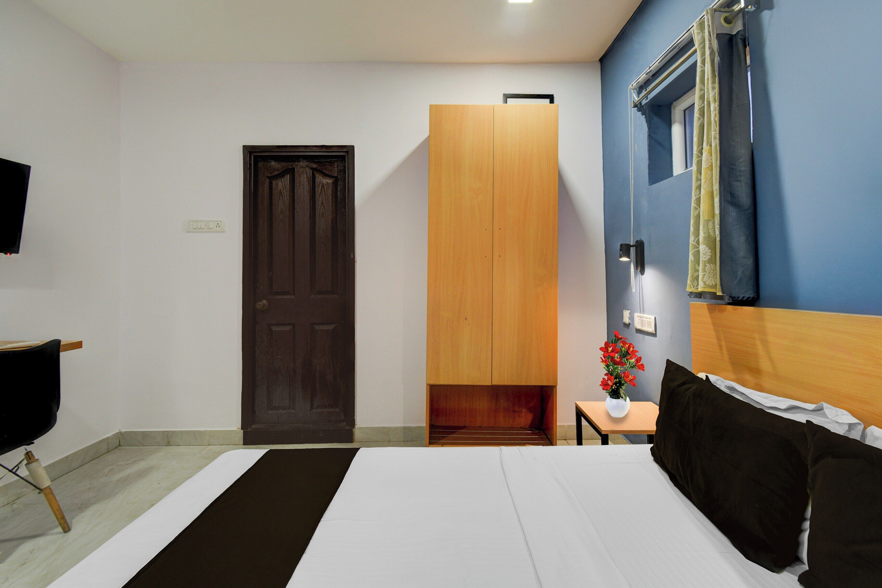 Habitación de hotel con cama, armario de madera, una mesita con un florero y televisor en la pared.