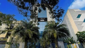 Um edifício moderno com fachada de vidro, cercado por palmeiras e uma cerca de metal.