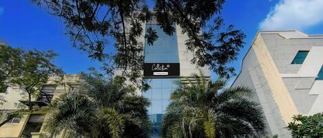 A modern building with a glass facade, surrounded by palm trees and a metal fence.