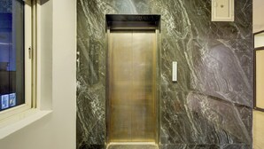Um elevador com interior metálico, rodeado por paredes de mármore com um padrão de veios.