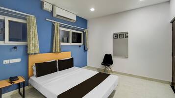 Habitación de hotel con cama, escritorio, silla, equipo de aire acondicionado y ventana con cortinas.