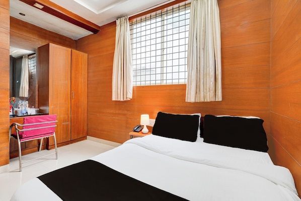 A hotel room with a bed, a bedside table with a lamp, a mirror, a wardrobe, and a window with curtains. - Collection O Kalyan Nagar Bangalore (Bengaluru)