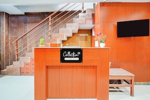 A reception desk with a sign indicating it's a company-serviced collection point, a staircase, and a wall-mounted television. - Collection O Kalyan Nagar Bangalore (Bengaluru)