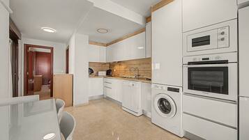 Een moderne keuken met witte kasten, een accentmuur van hout, een ingebouwde wasmachine en een magnetron.