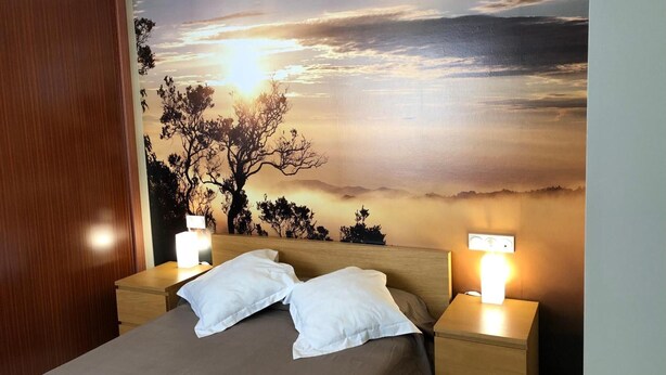 A bedroom with a bed, two bedside tables, and a wall mural of a sunset.