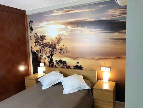 A bedroom with a bed, two bedside tables, and a wall mural of a sunset.