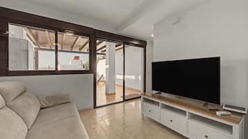A living room with a large flat-screen TV, a beige sofa, and a sliding glass door leading to an outdoor area.
