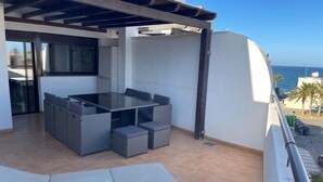A balcony with a glass-top table and chairs, a view of the sea, and a tiled floor.