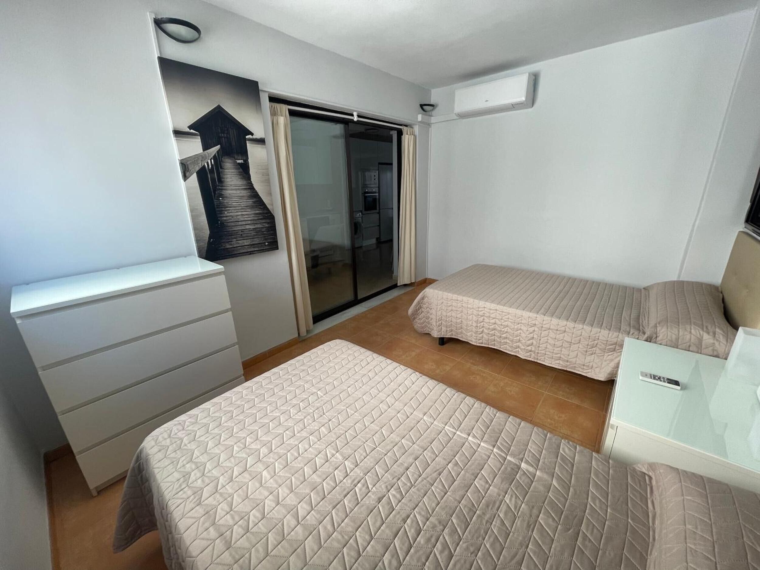 Ein Hotelzimmer mit zwei Betten, einem Schreibtisch, einem Stuhl, einer Schiebetür und einer Wand-Klimaanlage.