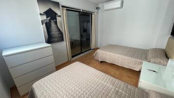 Ein Hotelzimmer mit zwei Betten, einem Schreibtisch, einem Stuhl, einer Schiebetür und einer Wand-Klimaanlage.