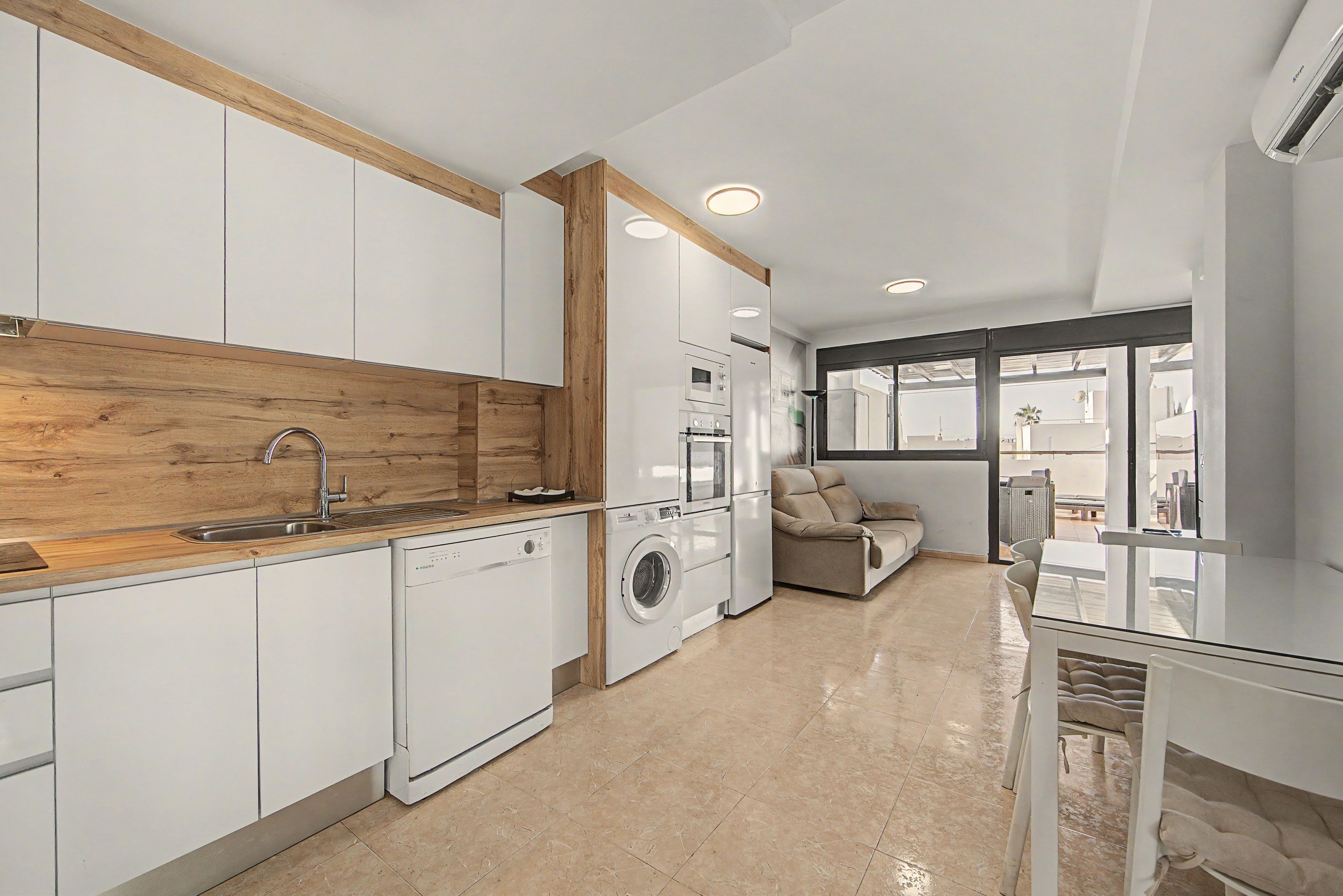 Een moderne keuken met inbouwapparatuur, een wand bekleed met hout en een zithoek met een bank en tafel.