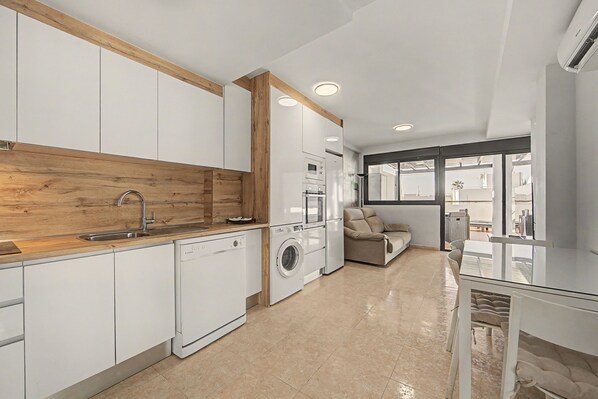 A modern kitchen with built-in appliances, a wooden accent wall, and a dining area with a sofa and table.