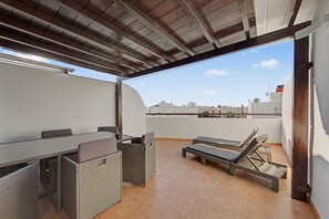 Una terraza en la azotea con mesa y sillas, un sillón de sol y vistas panorámicas de la ciudad.