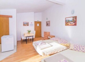 Ein Zimmer mit einem Bett, einem Sessel, einem Tisch, einer Kommode und einem Kühlschrank.