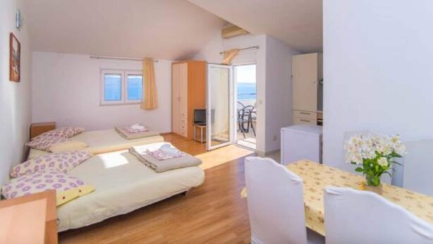 Ein Schlafzimmer mit einem Bett, einem Schreibtisch und einem Stuhl. Ein Fenster und eine Tür führen auf einen Balkon.