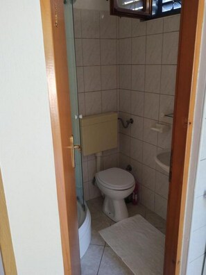 A small bathroom with a toilet, a sink, and a shower area. - Apartments Blaza - Studio Apartment (Vodice)