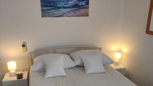 A hotel room with a bed, two bedside lamps, a painting of a seascape, and two rolled towels on the bed. - Apartments Blaza - Studio Apartment (Vodice)
