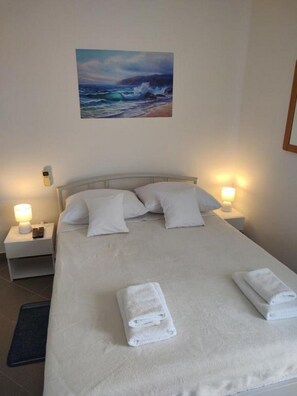 A hotel room with a bed, two bedside lamps, a painting of a seascape, and two rolled towels on the bed. - Apartments Blaza - Studio Apartment (Vodice)