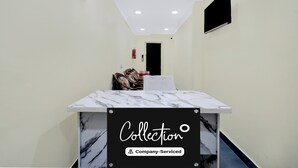 Un vestíbulo de hotel con mostrador de recepción, extintor, perchero y televisor montado en la pared.
