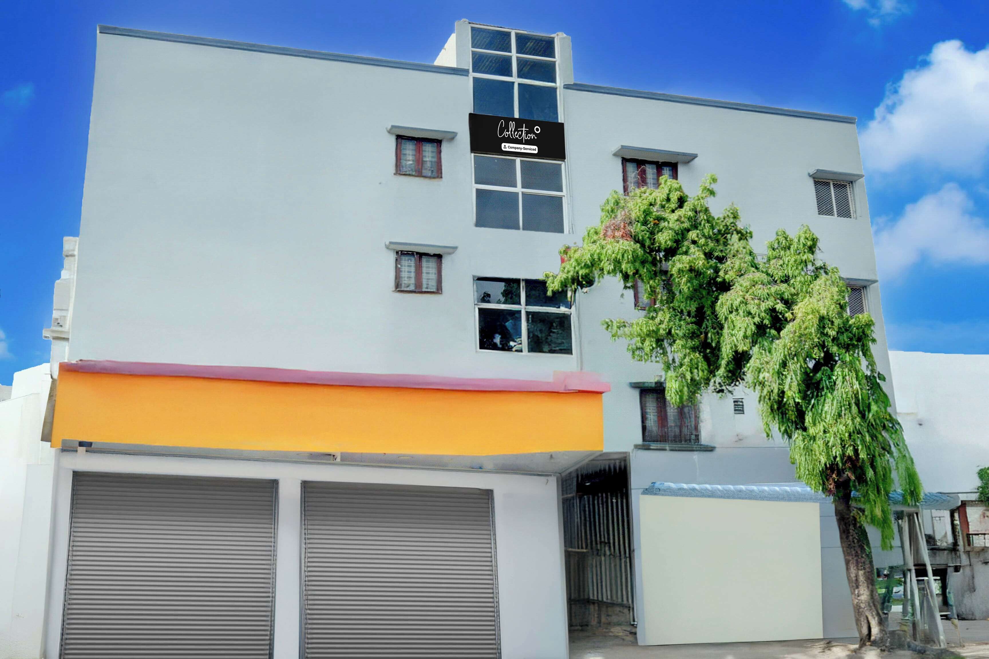 Un edificio de varios pisos con fachada plana, letrero de empresa y un árbol en frente.