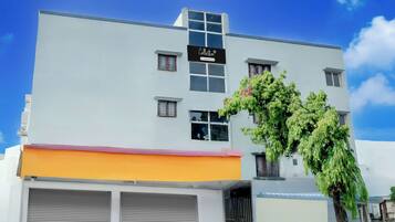 Un edificio de varios pisos con fachada plana, letrero de empresa y un árbol en frente.