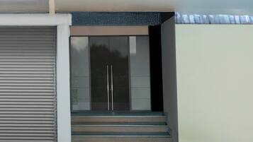 A set of stairs leading to a door with a glass panel, a closed roller shutter to the left, and a plain wall above.