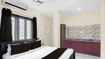 Une chambre d’hôtel équipée d’un lit, d’un climatiseur, d’un ventilateur de plafond, d’une fenêtre avec des rideaux, d’une œuvre d’art accrochée au mur et d’un pare-feu en carreaux.