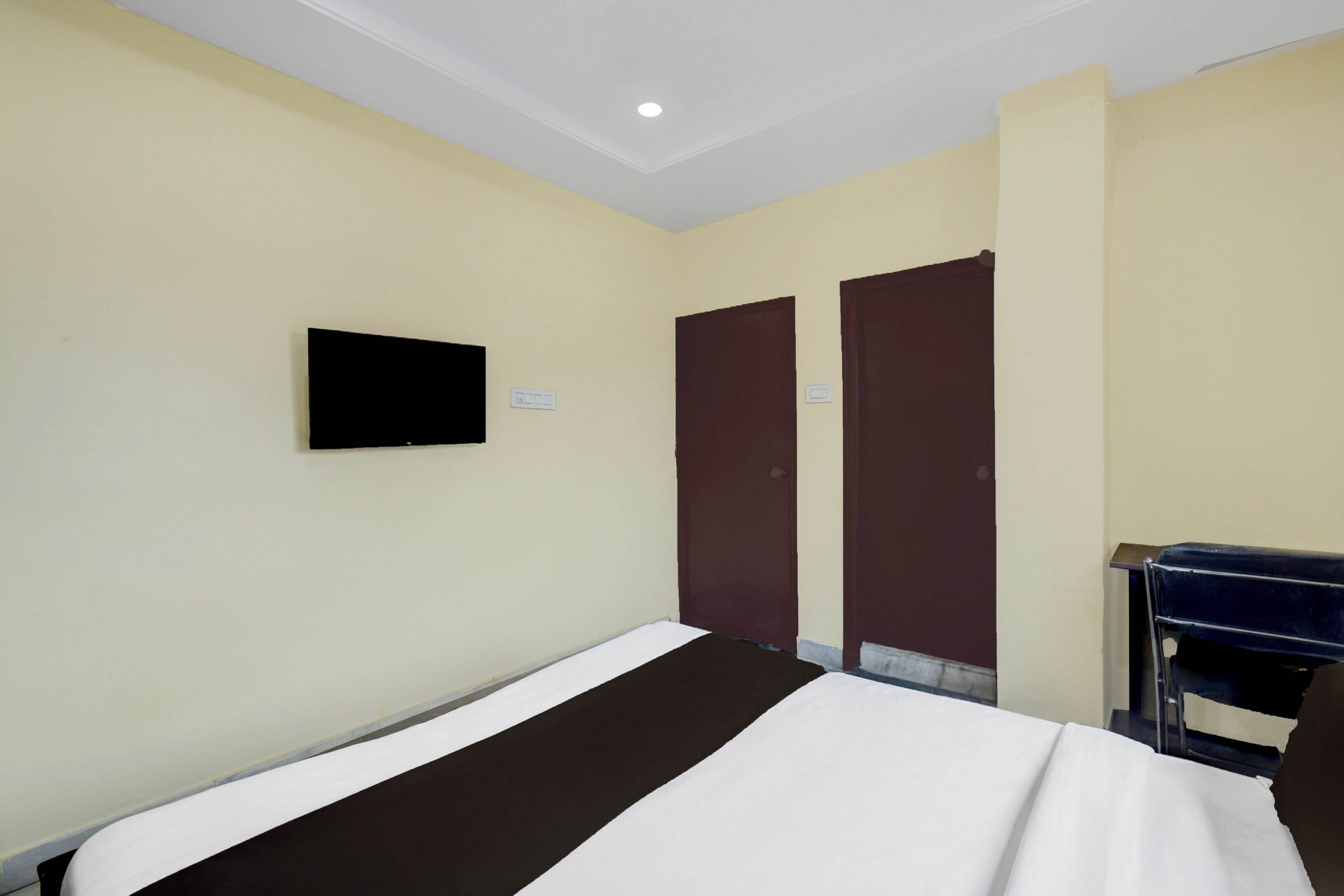 A hotel room with a bed, a desk, two doors, and a television on the wall.