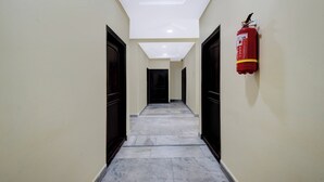 Un pasillo con extintor montado en la pared, puertas a ambos lados y suelo de baldosas.