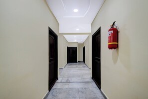 A hallway with a fire extinguisher mounted on the wall, doors on both sides, and a tiled floor.