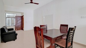 Un comedor con mesa y sillas de madera, ventilador de techo y sofá negro.