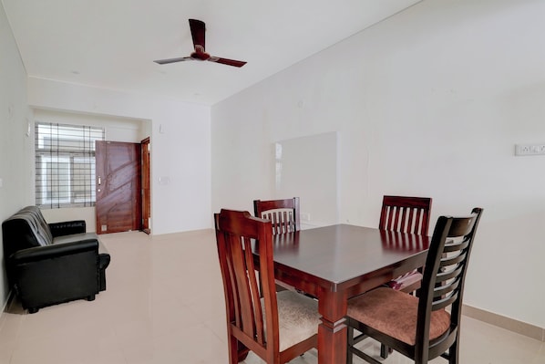 A dining area with a wooden table and chairs, a ceiling fan, and a black sofa. - Collection O REVA University Rukmini (Bangalore)