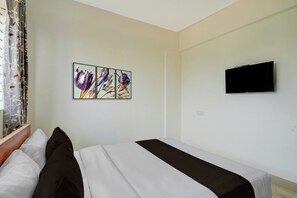 A hotel room with a bed, a flat-screen TV mounted on the wall, and a set of three framed floral paintings above the bed. - Collection O REVA University Rukmini (Bangalore)