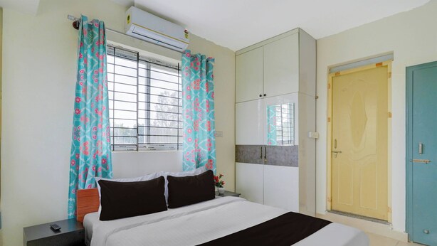 Un dormitorio con cama, mesita de noche, ventana con cortinas, aire acondicionado, armario y puerta.
