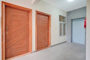 A hallway with two wooden doors, a window with a grid pattern, and a red fire extinguisher mounted on the wall. - Collection O REVA University Rukmini (Bangalore)