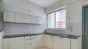 Una cocina con armarios blancos, una encimera negra, una ventana con barrotes y una puerta verde.