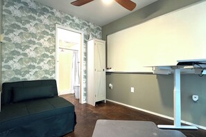 Ein Zimmer mit einem dunkelgrünen Sofa, einem weißen Schrank, einer grauen Bank und einem Deckenventilator.